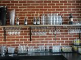 un mur de briques derrière le bar, avec des verres à vin sur les étagères