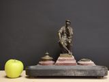 a statue of a man sitting on top of a table next to an apple