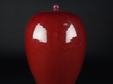 un vase rouge avec un couvercle rose posé sur une surface noire
