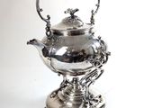 une théière ancienne en argent posée sur un socle, sur fond blanc