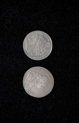 two silver coins sitting side by side on a black surface