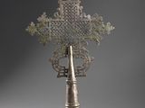 une vieille croix en argent posée sur un vase en argent, sur un fond gris