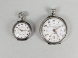 two silver pocket watches sitting next to each other on a white surface