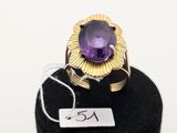 un gros plan d'une bague sertie d'une pierre violette, posée sur un socle