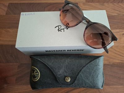 Lunettes de soleil Ray-Ban dans leur boîte et leur étui, posées sur un plancher en bois