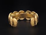 a close up of a gold cuff bracelet on a black background