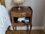 a small table with a lamp on it next to a bed
