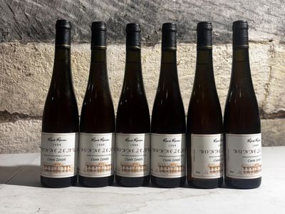 six bottles of wine are lined up on a table in front of a stone wall