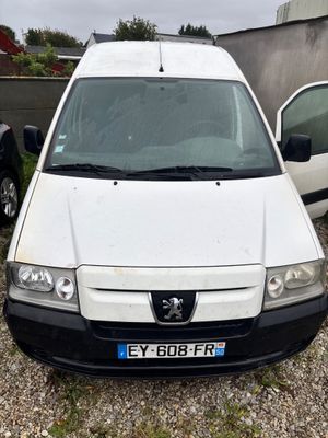 La petite camionnette blanche est garée sur un parking, à côté d'autres voitures.