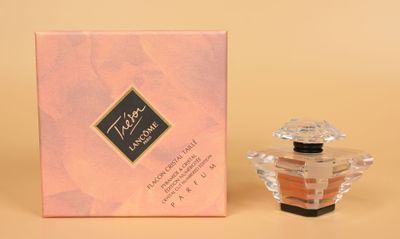 un petit flacon de parfum posé à côté d'une boîte rose