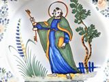 a plate with a painting of a saint holding a staff