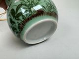 a person holding a green vase with a painting on it