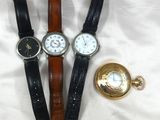 trois montres et une montre de poche posées sur un lit recouvert d'un drap blanc