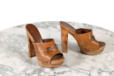 des mules en cuir de style « clogger » à talon en bois et boucles, posées sur une table en marbre