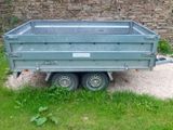 a trailer that is sitting in the grass near a stone wall