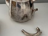 a silver tea pot sitting next to a cup on a table