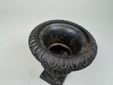 a black vase on a stand on a white surface