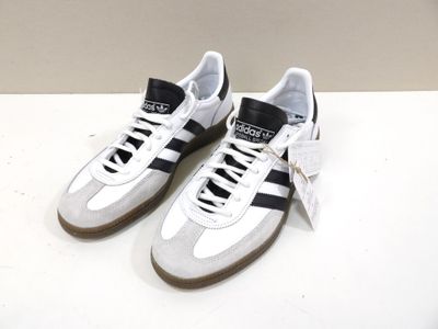 Des baskets adidas à rayures noires et blanches sont posées sur une surface blanche