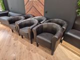 Quatre fauteuils en cuir noir sont alignés en rang devant un mur.
