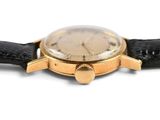 a gold watch on a black strap on a white surface