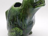 un vase en forme de grenouille verte posé sur une surface blanche