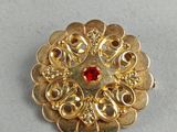a close up of a gold brooch with a red stone in the center