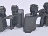 three black binoculars are lined up on a white surface