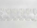 six clear wine glasses lined up in a row on a white surface