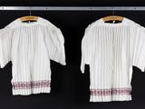 two white blouses hanging on a black wall with a wooden hanger