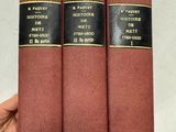 Une main tient trois livres rouges à la couverture noire