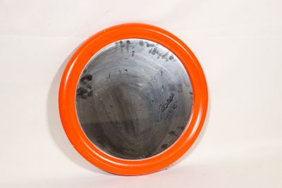 un miroir rond orange accroché à un mur blanc