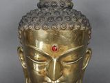 une tête de Bouddha en or surmontée d'une pierre rouge