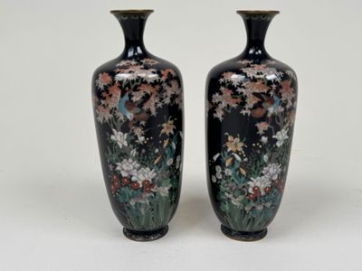 two black vases with flowers on them on a white surface