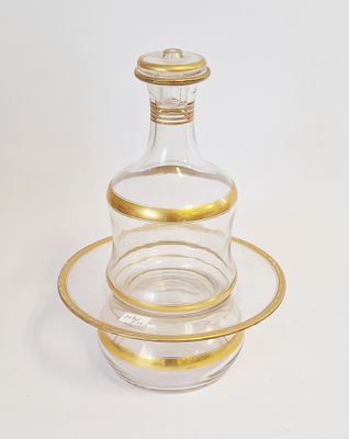 une carafe en verre ancienne, bordée d'or, posée sur une soucoupe