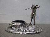 une statue en argent représentant un homme tenant un club de golf, assis sur un rocher
