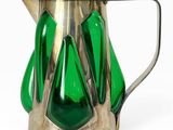 un pichet en verre vert muni d'une anse en métal, posé sur une surface blanche
