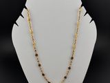 un collier à chaîne en or orné de perles noires, porté par un mannequin blanc
