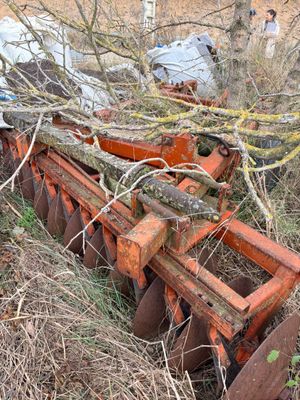 a tractor that is sitting in the grass with a plow behind it