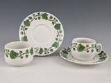 two cups and saucers with green leaves on them sitting on a table