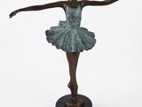La statue en bronze d'une ballerine se dresse sur un socle noir.