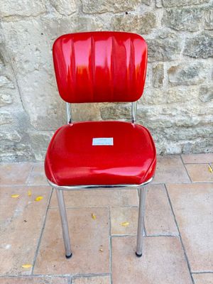 une chaise rouge sur laquelle est posée une étiquette, placée devant un mur de pierre
