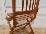 une chaise pliante en bois assise sur le sol devant un mur blanc