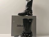 une paire de bottes en cuir noir ornées de chaînes, posée sur une boîte