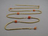 three gold chain necklaces with orange beads on a gray surface