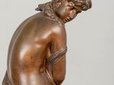 bronze statue of a boy sitting on a rock with his hands on his knees