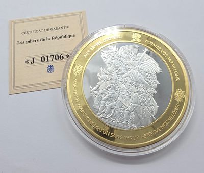 une pièce de monnaie argentée et dorée posée sur une surface blanche, à côté d’une carte