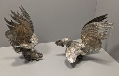 paire de figurines anciennes en argent plaqué représentant des coqs, posées sur une table blanche