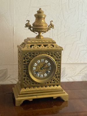 a gold clock on a wooden table with a white wall in the background