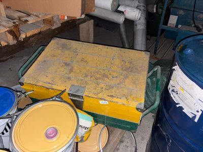 une boîte jaune posée sur une table, à côté de deux fûts bleus