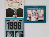 trois livres posés sur un mur blanc, sur lesquels figurent des photos d'hommes et de femmes